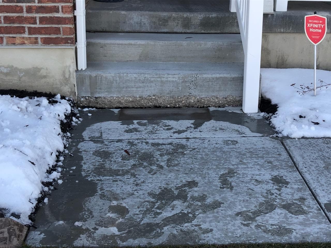 Concrete sidewalk with snow and ice, residential stairs in the background.