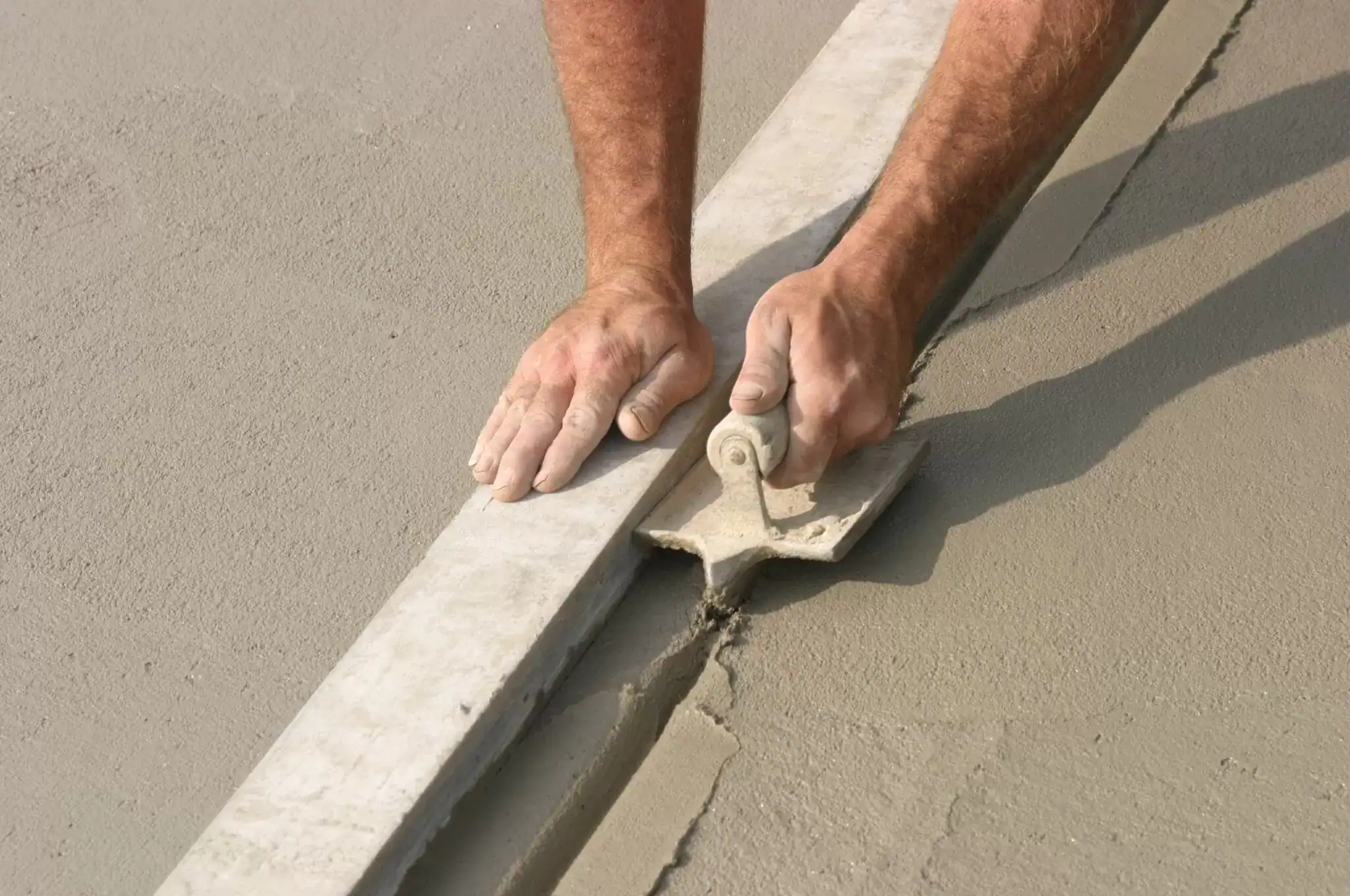 Worker smoothing freshly poured concrete with a trowel for a level surface.